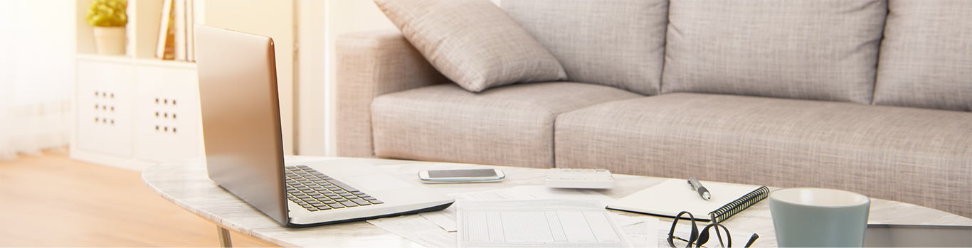 clean modern livingroom with a couch, a laptop, a notbook, a smartphone, and a pair of glasses on the coffee table