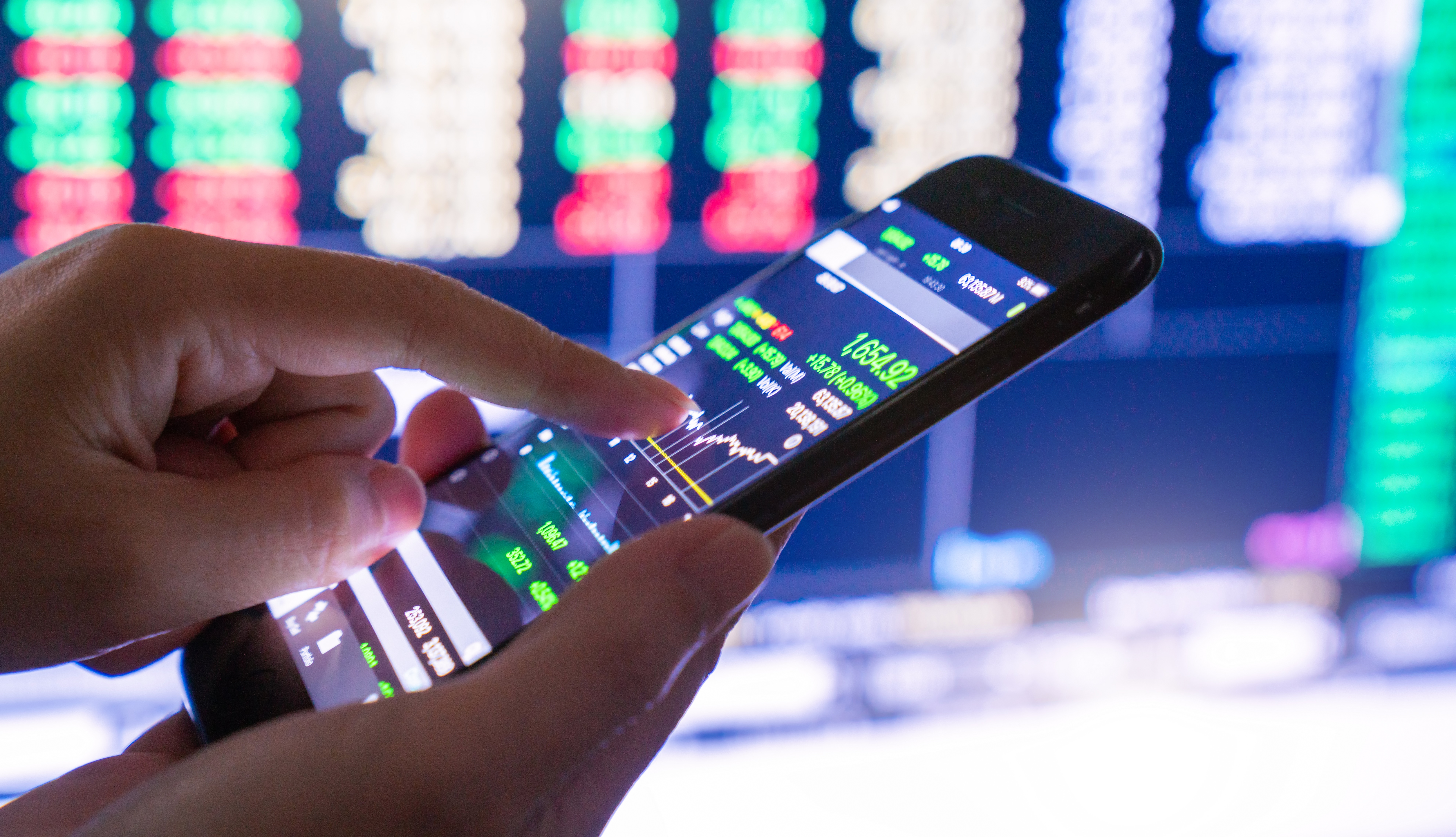Close up of a phone and a person touching the screen. The screen displays stock market information.